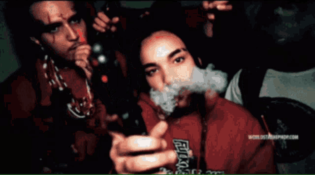 a woman smoking a cigarette next to a man wearing a red shirt that says ' worldstarhiphop.com ' on it