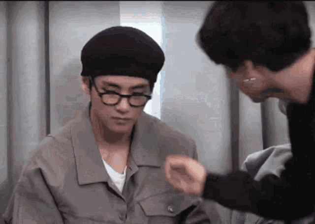 a man wearing glasses and a hat is talking to another man .