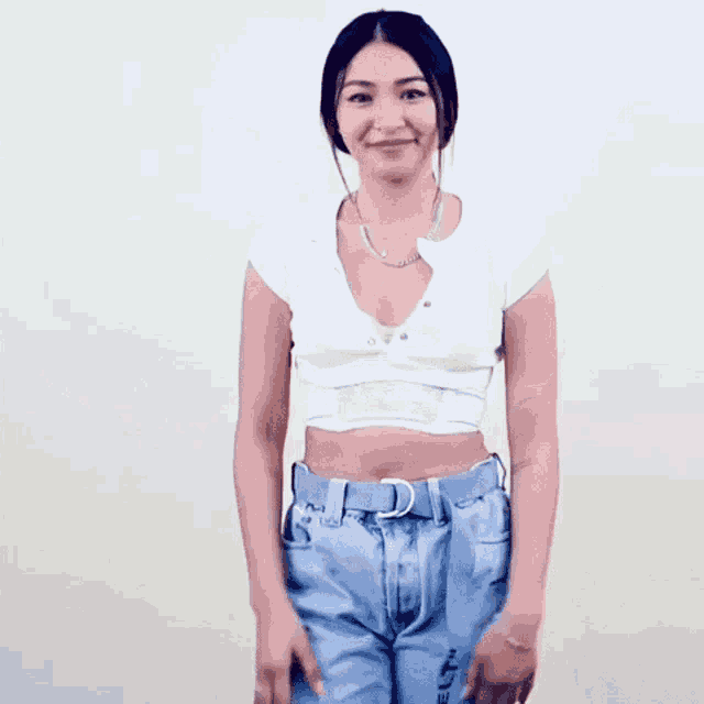 a woman in a white crop top and blue jeans is dancing .