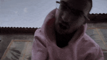 a man wearing glasses and a pink hoodie is looking down