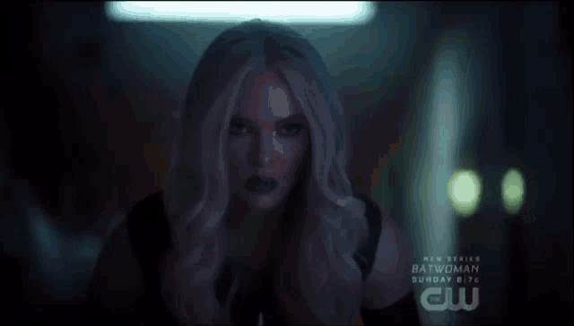a woman in a dark room with a new series batwoman advertisement behind her