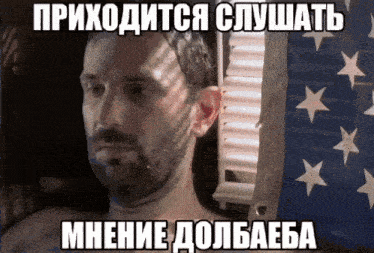 a man with a beard is laying in front of an american flag with russian writing