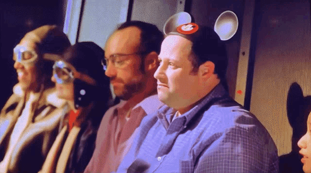 a man wearing a mickey mouse headband sits in a row of people