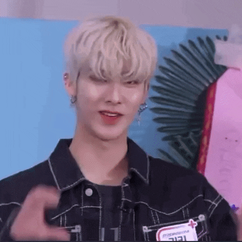 a young man with blonde hair and earrings is making a heart shape with his hand .