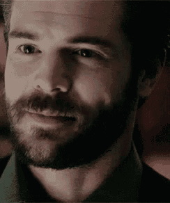 a close up of a man with a beard smiling and looking at the camera .