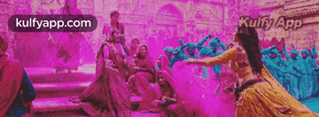 a woman in a yellow dress is dancing in front of a crowd of people covered in purple powder .