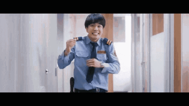 a security guard in a blue uniform and tie is walking down a hallway and smiling .