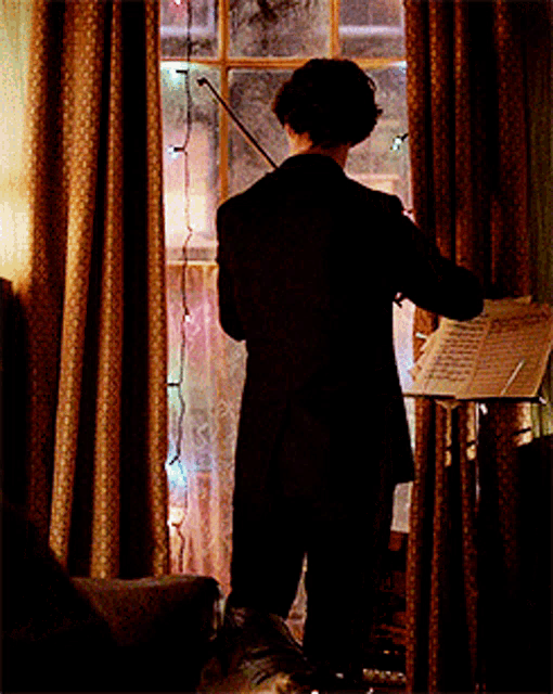 a man playing a violin in front of a window with christmas lights