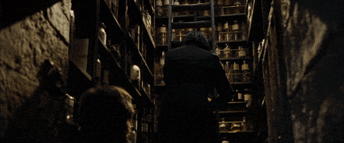 a man standing in a dark room with shelves full of bottles and jars