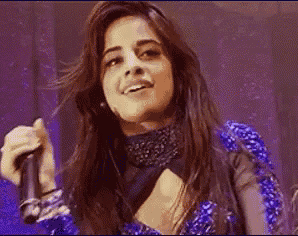 a woman is singing into a microphone on a stage while wearing a blue dress .