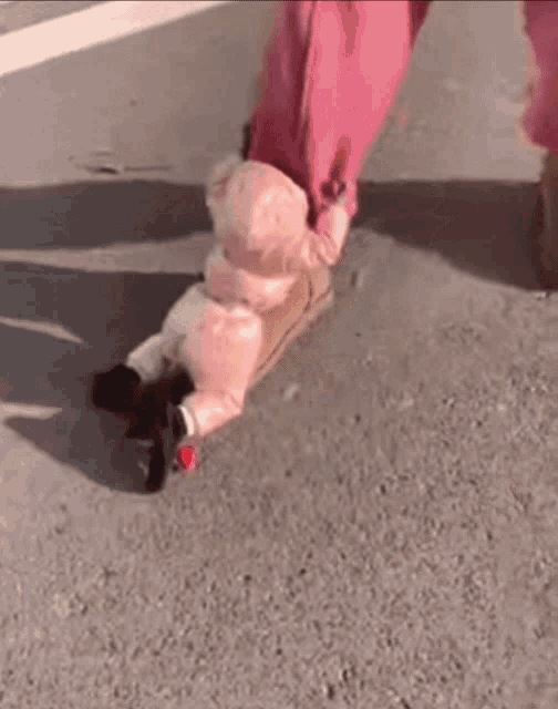 a baby in a pink jacket is being pulled by a person 's leg .