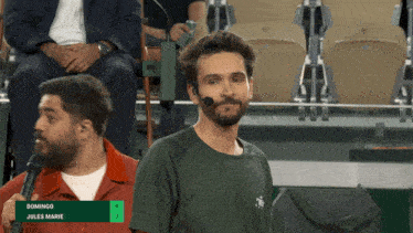 a man in a green shirt is speaking into a microphone with the name domingo jules marie below him