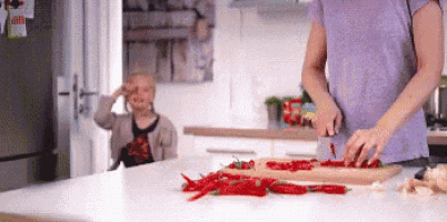 a woman is cutting up red peppers on a cutting board while a little girl watches .