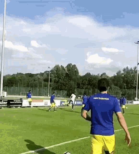 a man in a blue shirt with the word new balance on it is playing soccer on a field with other players .
