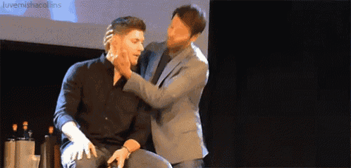 a man in a suit is touching another man 's face .
