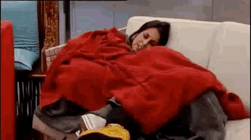 a woman is laying on a couch with a red blanket on her .