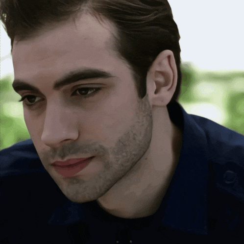 a close up of a man 's face with a beard wearing a blue shirt