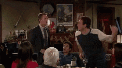 a man in a suit and tie is standing in front of a group of people in a living room .