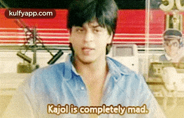 a man in a blue shirt is sitting in front of a microphone and saying kajol is completely mad .