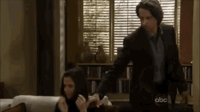 a man in a suit and tie is standing next to a woman on a couch with abc written on the bottom right