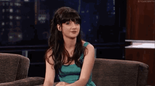 a woman in a green dress is sitting on a couch with her legs crossed .