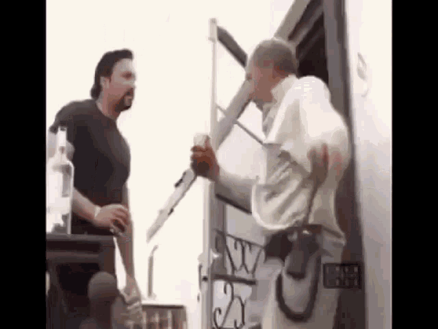 two men are standing next to each other in front of a trailer . one of the men is holding a cup of coffee .