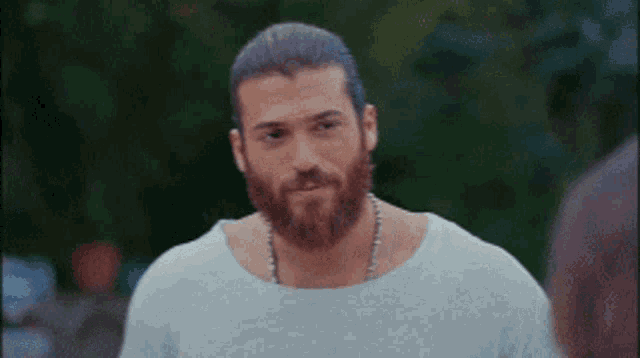 a man with a beard is wearing a white t-shirt and a necklace .