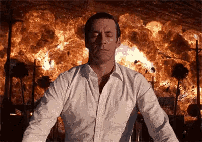 a man in a white shirt is standing in front of a fire
