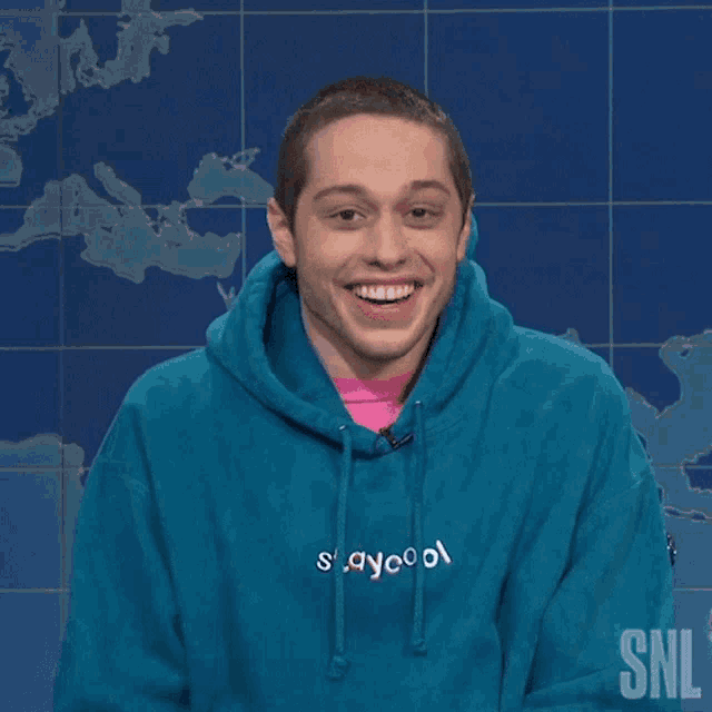 a man wearing a blue hoodie and a pink shirt is smiling for the camera .