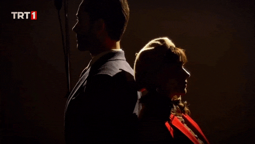 a man and a woman are standing back to back with the trt1 logo in the corner