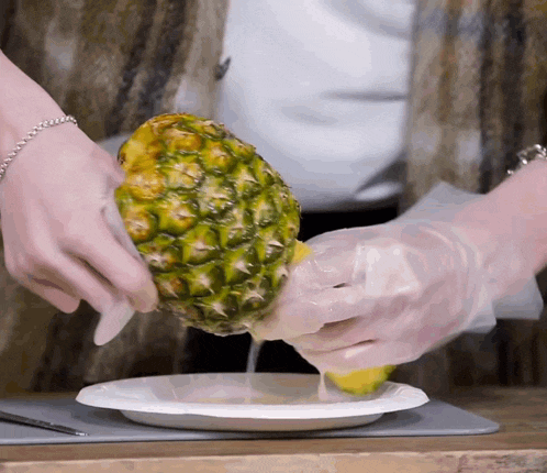 a person wearing plastic gloves is holding a pineapple on a paper plate
