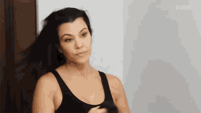 a woman in a black tank top is blow drying her hair