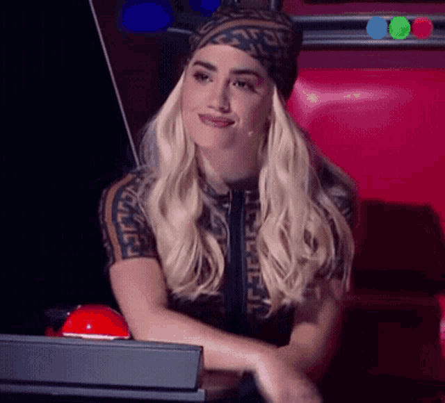a woman wearing a fendi shirt sits in front of a red button