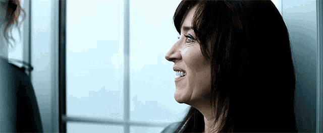 a woman is smiling and looking out a window while standing next to another woman .