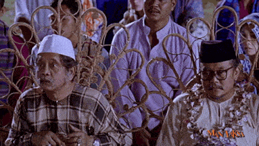 a man in a plaid shirt sits next to a man in a black hat with the word man laka on the bottom right