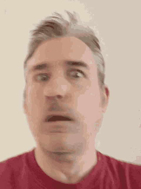 a man in a red shirt is making a funny face with his mouth open .