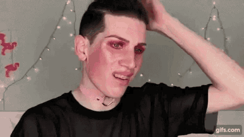 a young man with pink makeup on his face is wearing a black shirt .