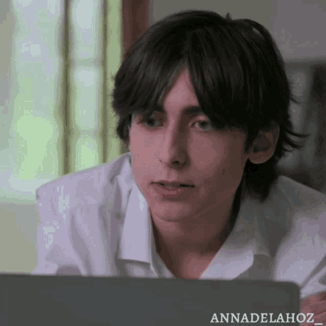 a young man in a white shirt is sitting in front of a laptop with the name annadelahoz on it