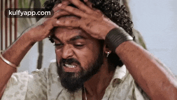 a man with a beard and curly hair is holding his head in his hands .