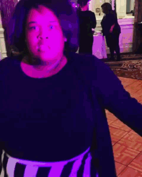 a woman in a black shirt is dancing with a purple light behind her