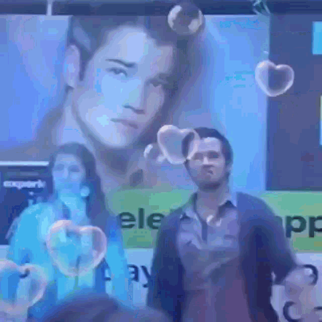 a man blowing soap bubbles in front of a poster of a man and a woman