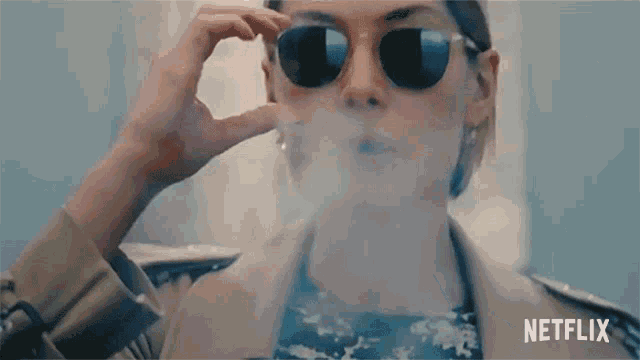 a woman wearing sunglasses is smoking a cigarette and the netflix logo can be seen in the corner
