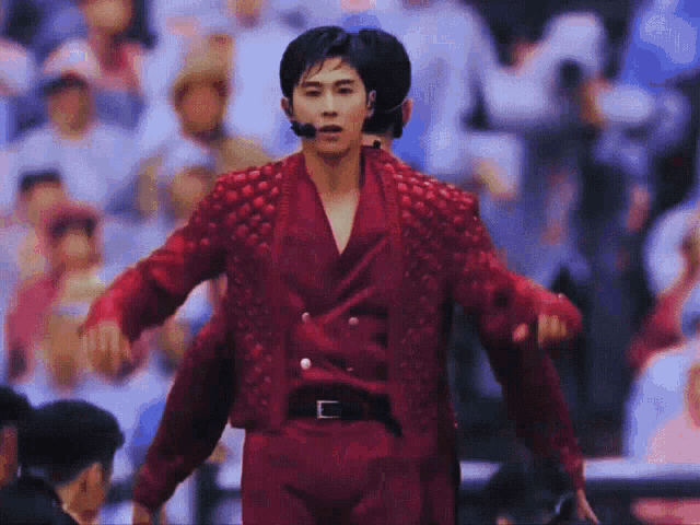 a man in a red jacket and pants is standing in front of a crowd with his arms outstretched