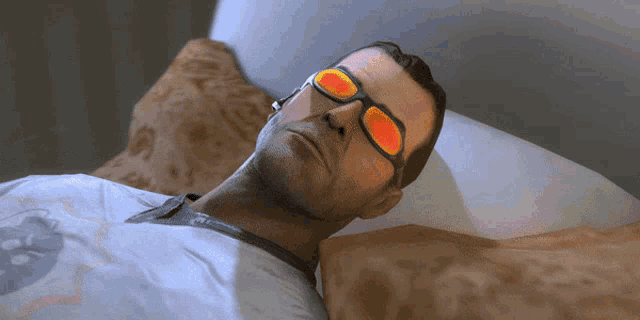 a man wearing sunglasses is laying in bed with his head on a pillow