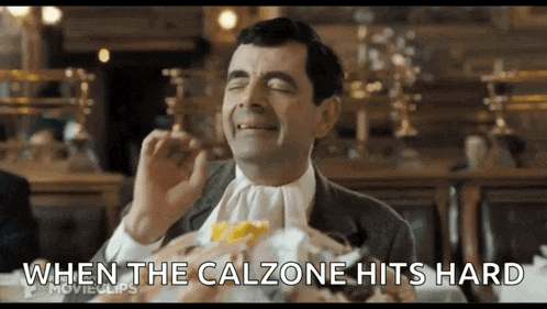 mr bean is sitting at a table eating a hamburger while wearing a white tie .