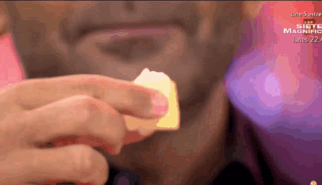 a close up of a man holding a piece of cheese with the words cine 5 estre on the bottom right
