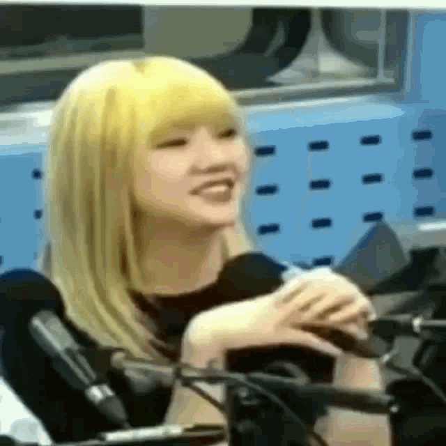 a young woman with blonde hair is sitting in front of a microphone and smiling .