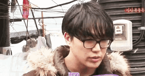 a young man wearing glasses and a fur hooded jacket is talking to someone .