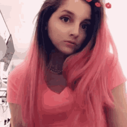 a young woman with pink hair is wearing a pink shirt and a flower in her hair .