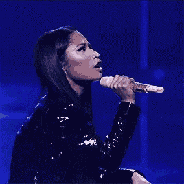 a woman in a black jacket is singing into a microphone .